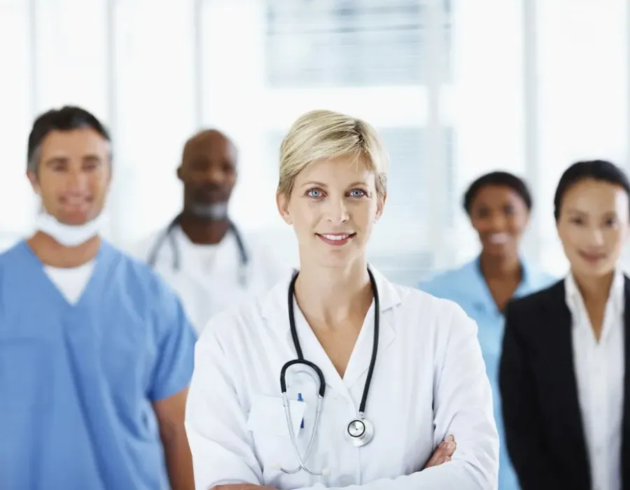 Healthcare manager in white coat smiling in front of group of healthcare staff and administrators